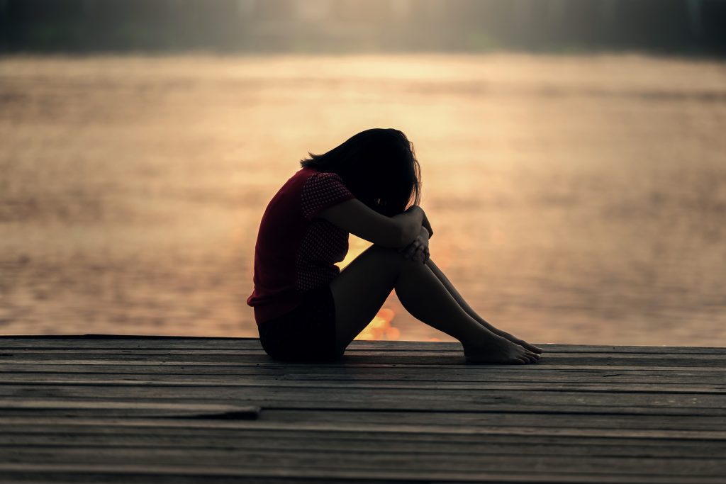 Person sitting alone by the water reflecting on loneliness