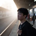 Young man standing alone at a train station feeling invisible as people pass by.
